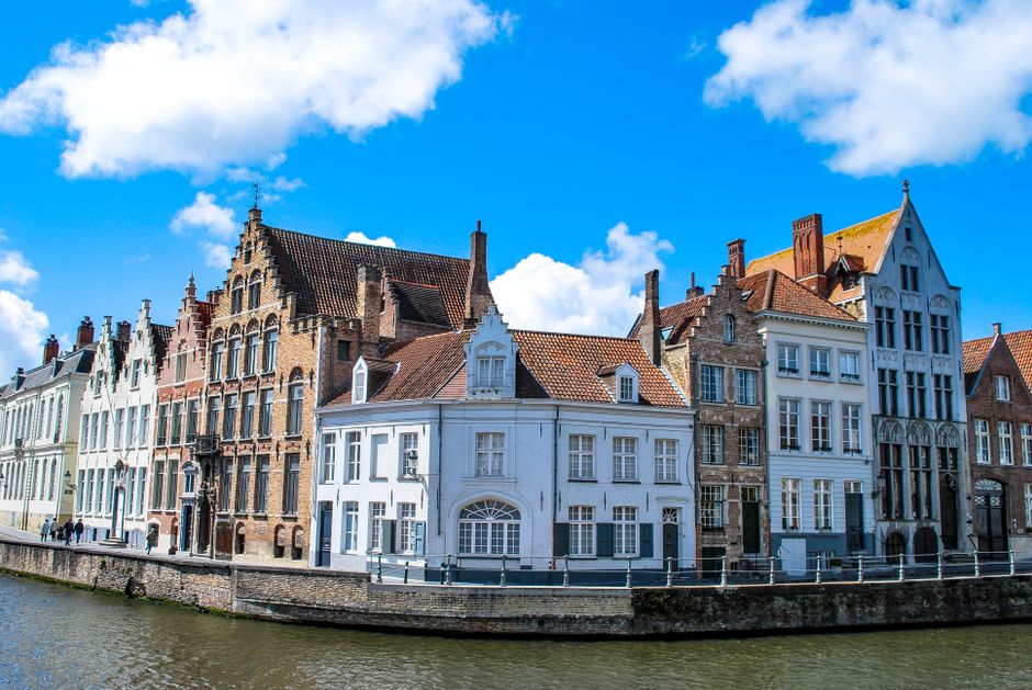 belgium — Charming townhouses along a canal in Bruges, Belgium under a vibrant blue sky.