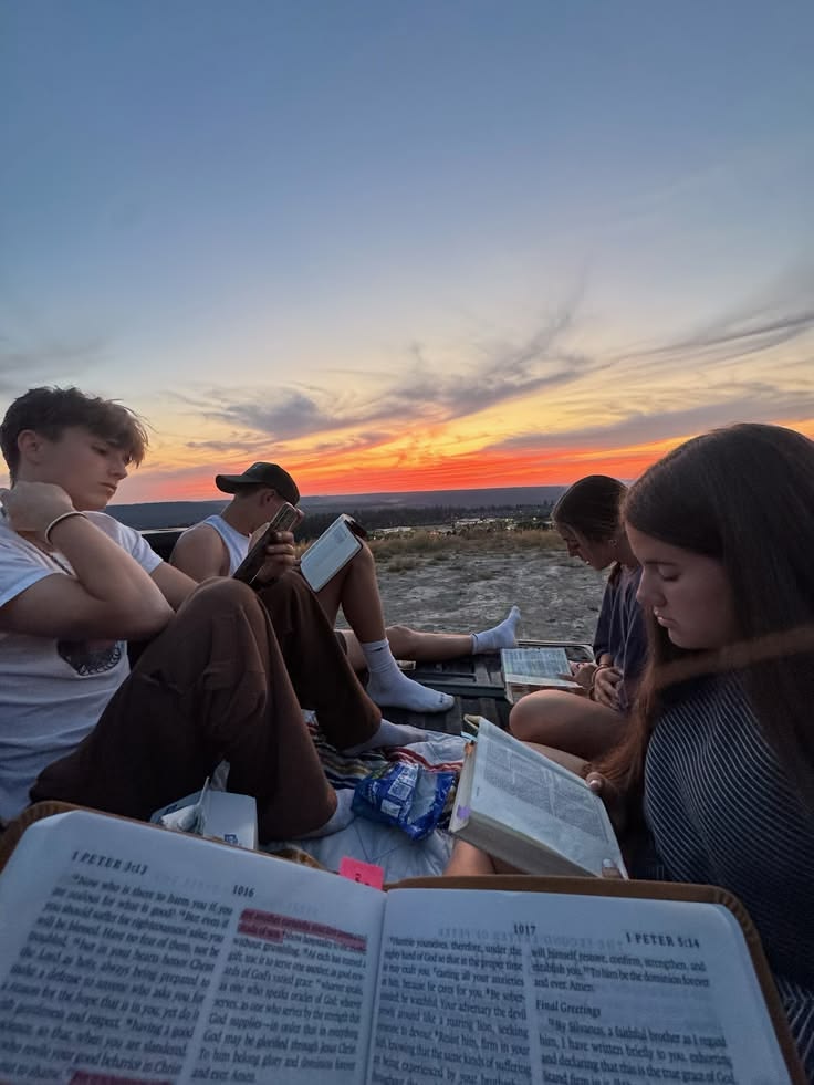Teens reading their Bibles together outdoors at sunset
