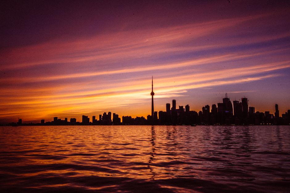 canada — Capture of Toronto's skyline with vibrant sunset colors reflecting on the water, featuring the iconi