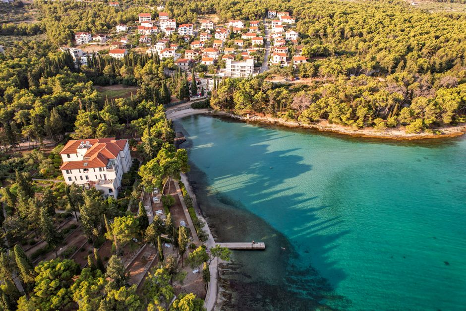 croatia — Aerial view of a picturesque coastal town surrounded by dense forests and clear turquoise waters.