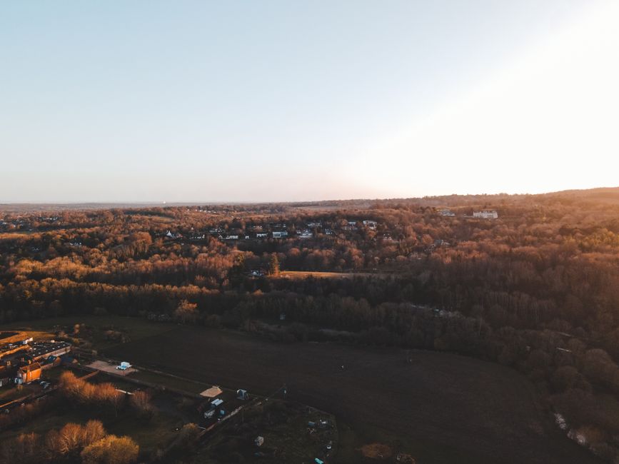 A scenic aerial shot over the English countryside at sunset showcasing houses and a vast forest.