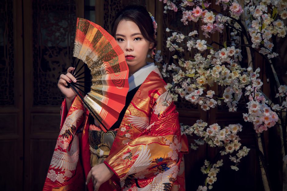 japan — An Asian woman in a vibrant kimono poses gracefully with a fan against a backdrop of sakura blossoms