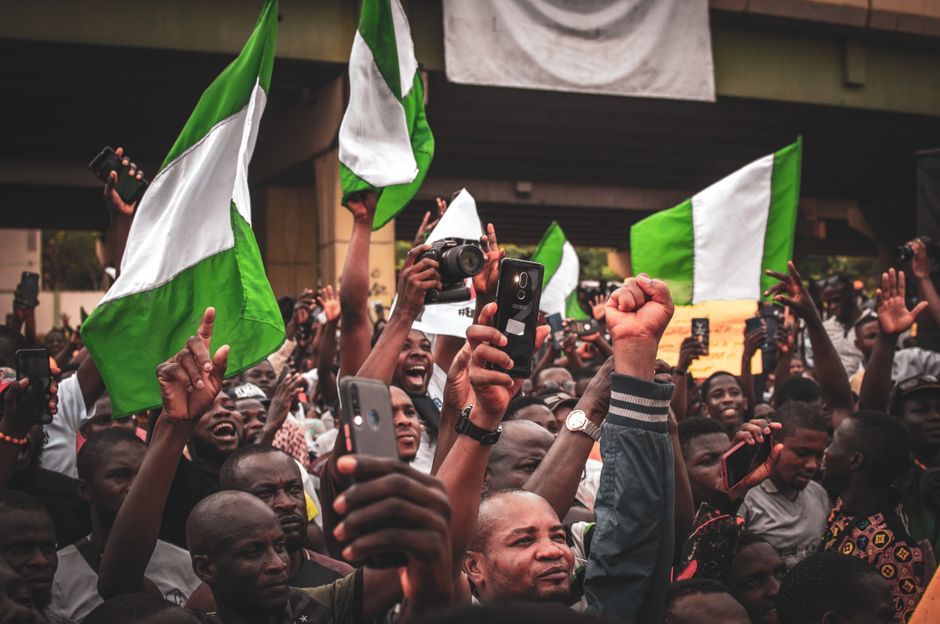 A lively street protest in Nigeria with activists waving flags and holding signs.