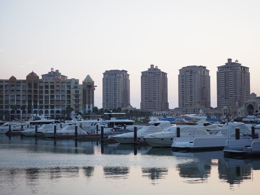 Beautiful evening view of luxury yachts at a marina in Doha, Qatar with tall buildings in the background.