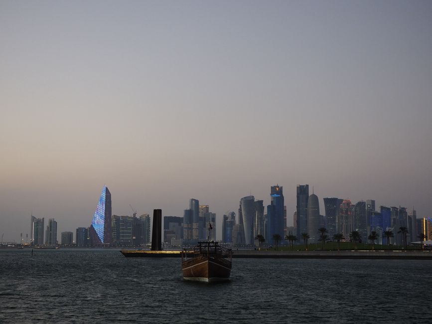 qatar — Scenic view of Doha city skyline with traditional dhow boat at dusk along the waterfront.