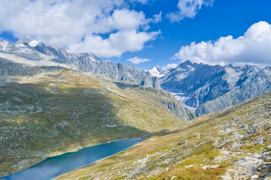 switzerland — A breathtaking view of the Swiss Alps with a tranquil lake and rugged mountain peaks under a vibrant