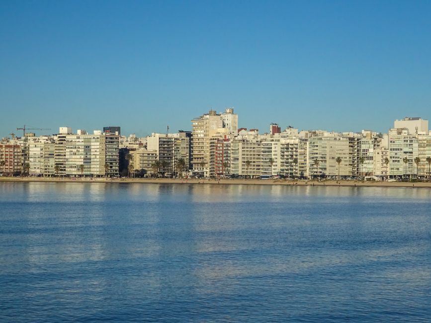 A serene view of Montevideo's skyline reflecting on the waterfront under a clear blue sky.