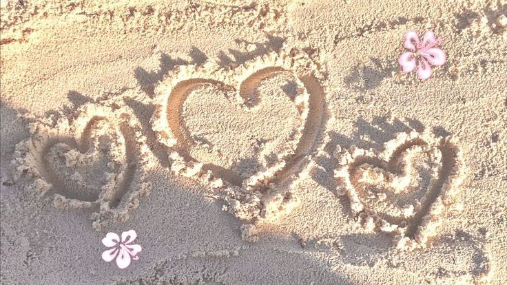Hearts drawn in soft beach sand with frangipani flowers